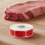 Top Round Steak Butcher sticker red identification label with black print on a roll of stickers with steak in background